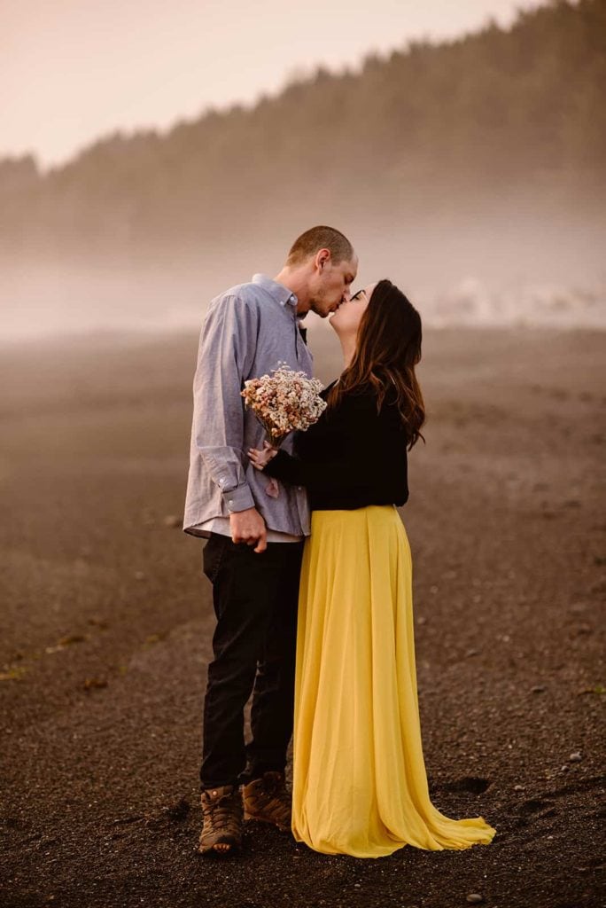 A man and woman share a kiss on the beach shore of Rialto in the Olympic Peninsula.