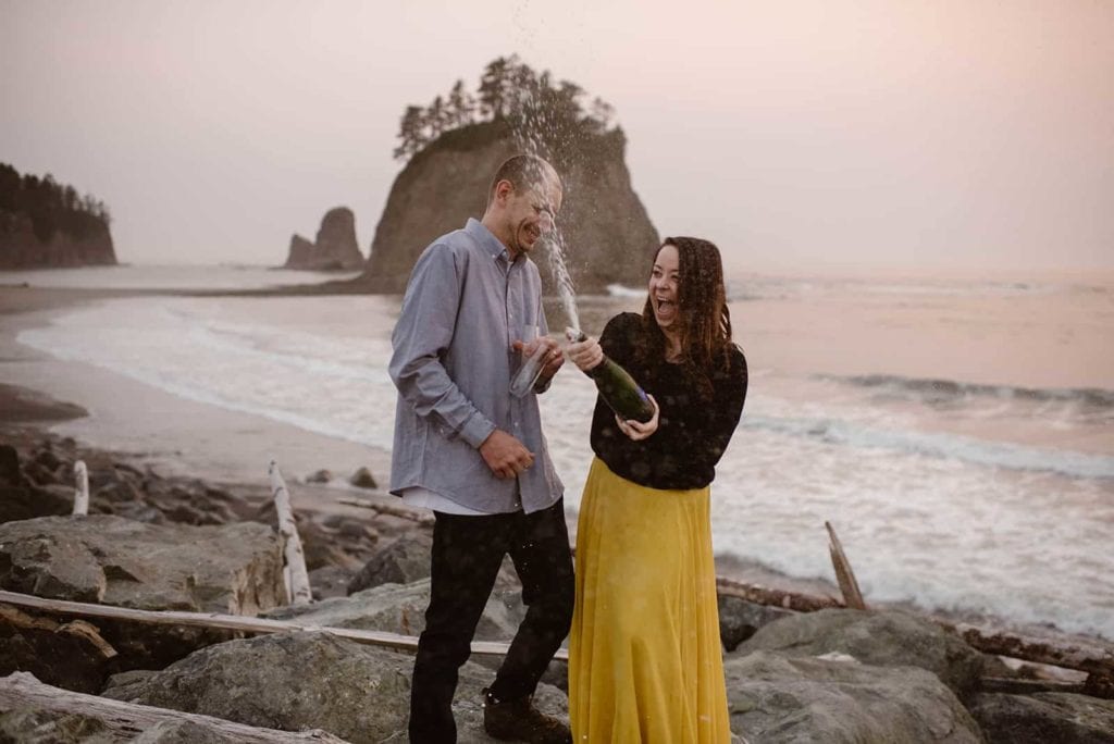 A couple sprays a bottle of champagne together on Rialto beach in celebration of their marriage earlier in the day.