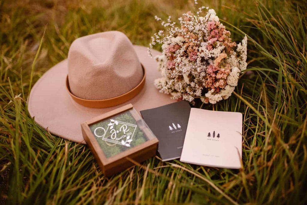 A hat laying in a grass field with a bouquet and wedding vow books.