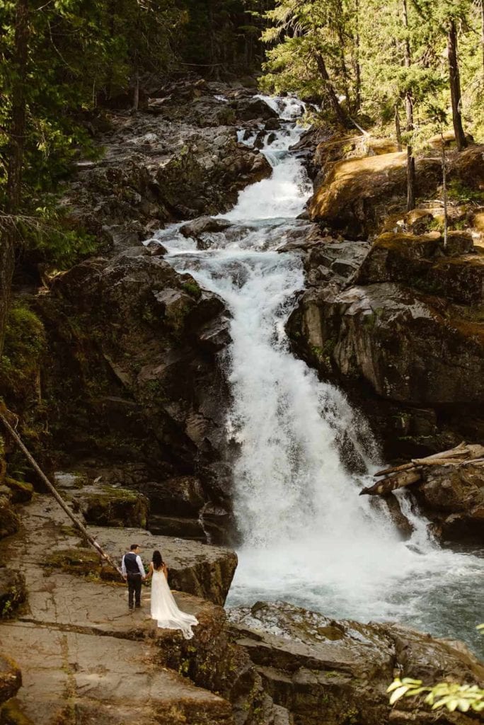 A couple stands at the base of a waterfall in Mt Rainier.
