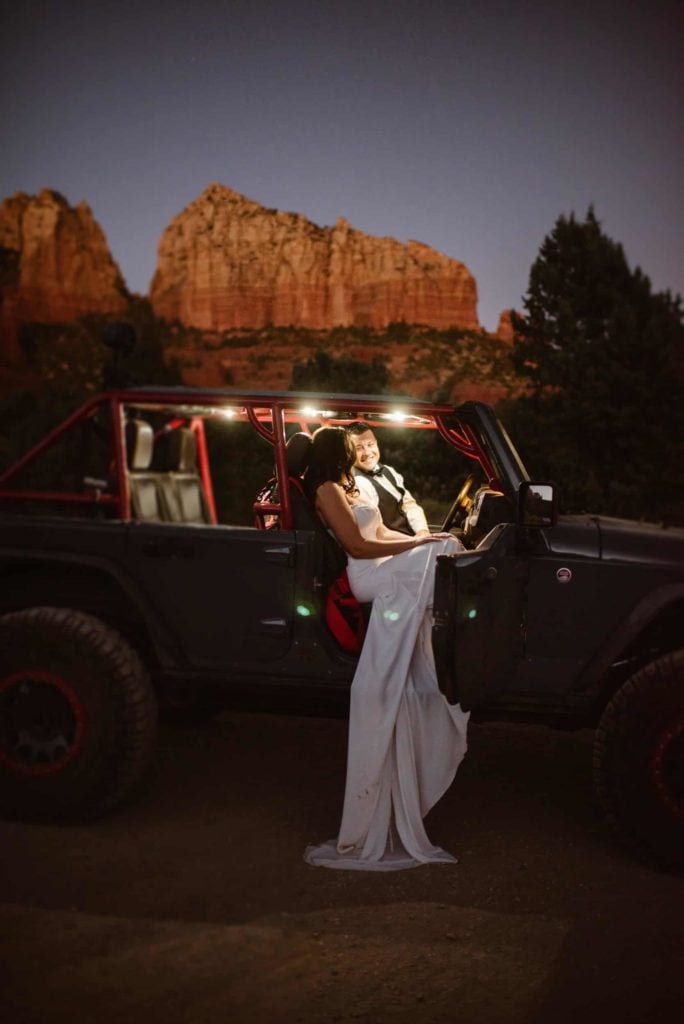 A groom smiles at his bride as they sit in a jeep together.