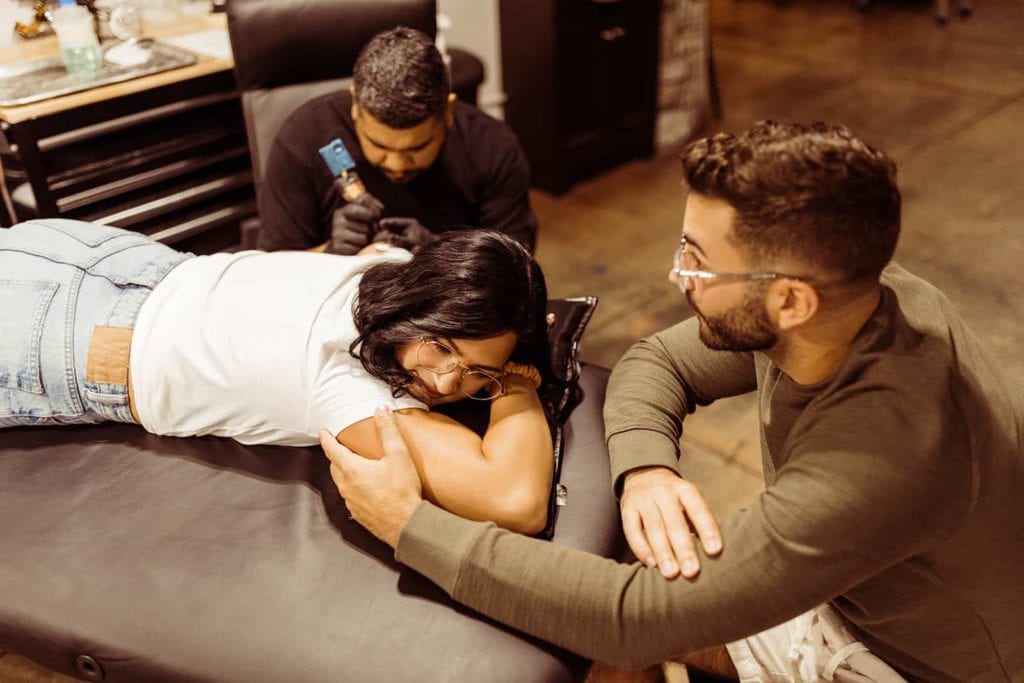 An engaged couple sit together to get a tattoo of their dog.