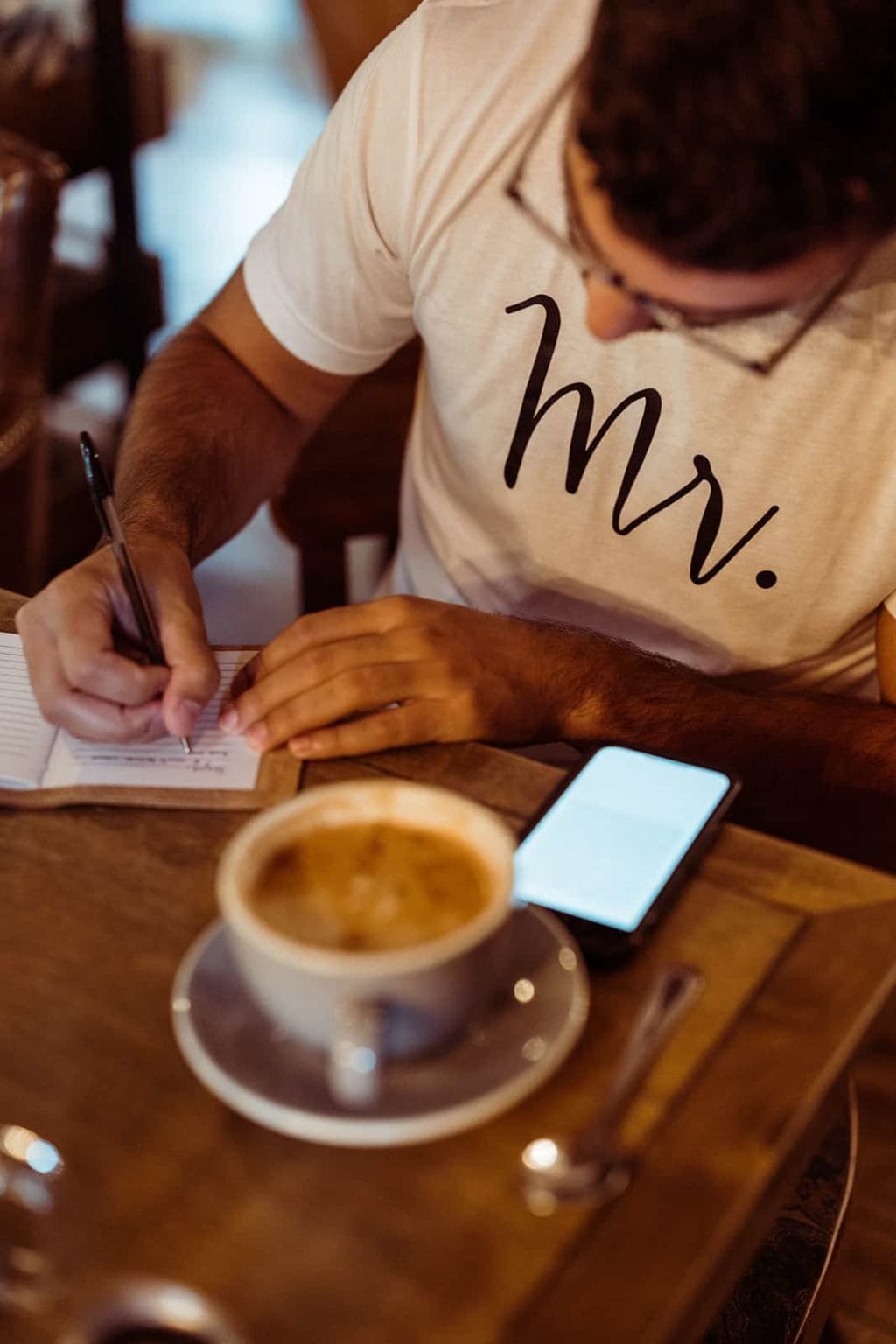 A groom writing his wedding vows while wearing a shirt that says Mr.