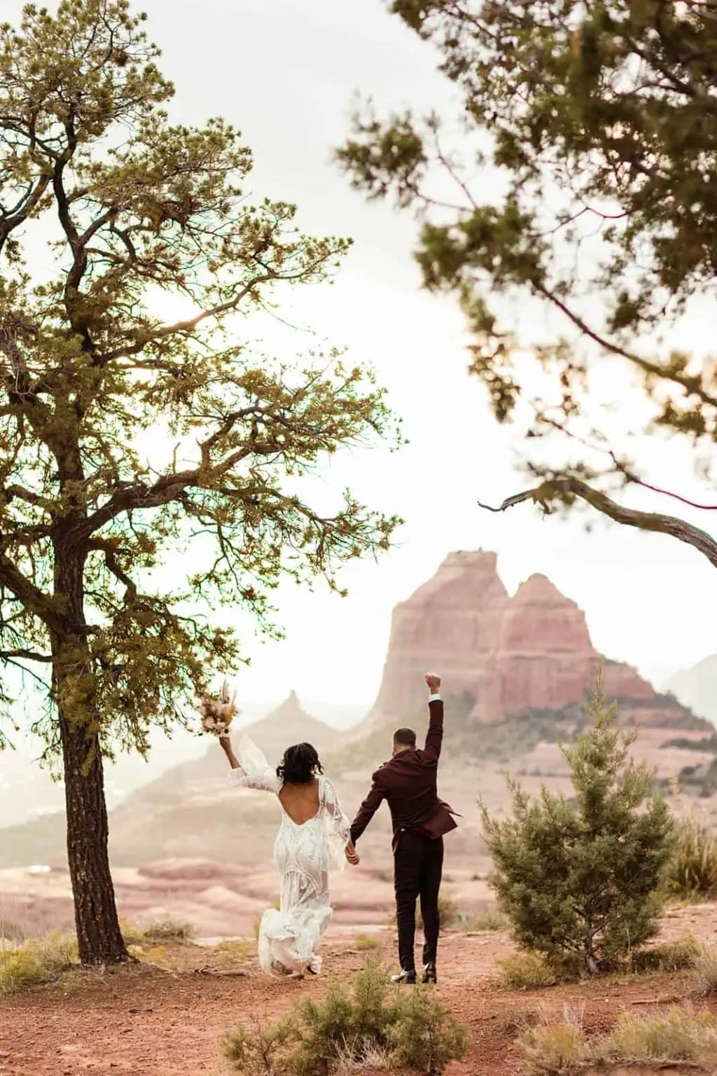 The bride and groom celebrate their ceremony as they walk towards the red rock views