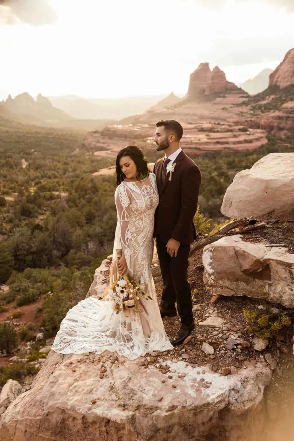 The bride and groom stand together on a limestone ledge with the sunset view of sedona behind them.
