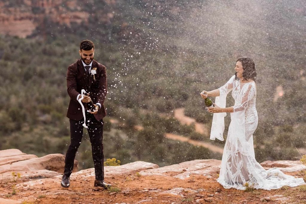 The bride and groom spray a bottle of champagne together among the red rocks of Sedona