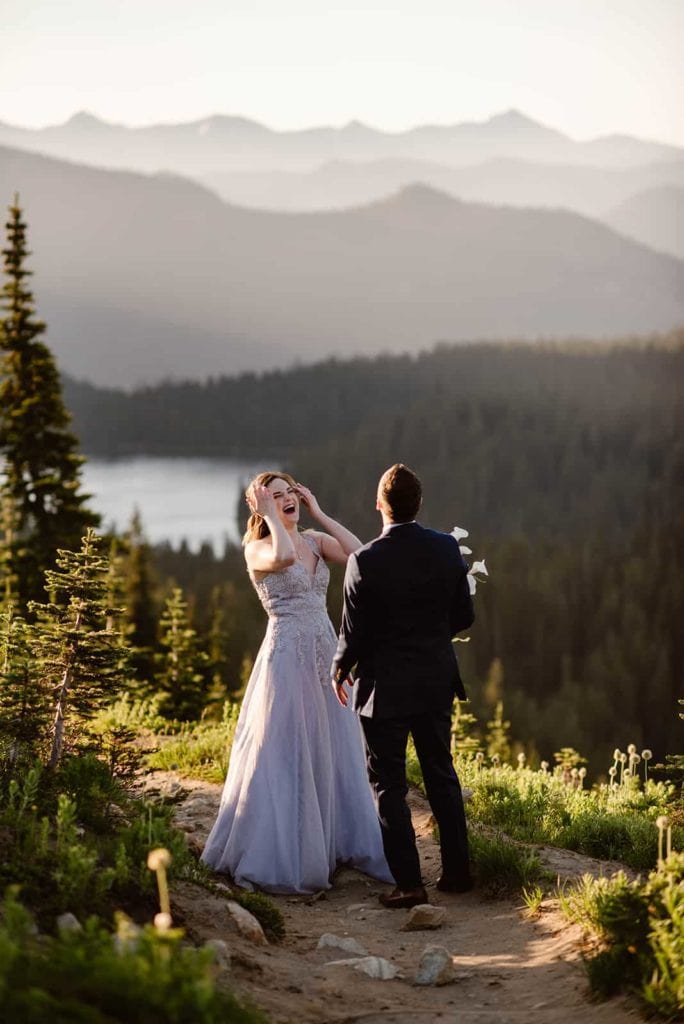 A bride laughs as she surprises her groom on trail with a second wedding dress. 