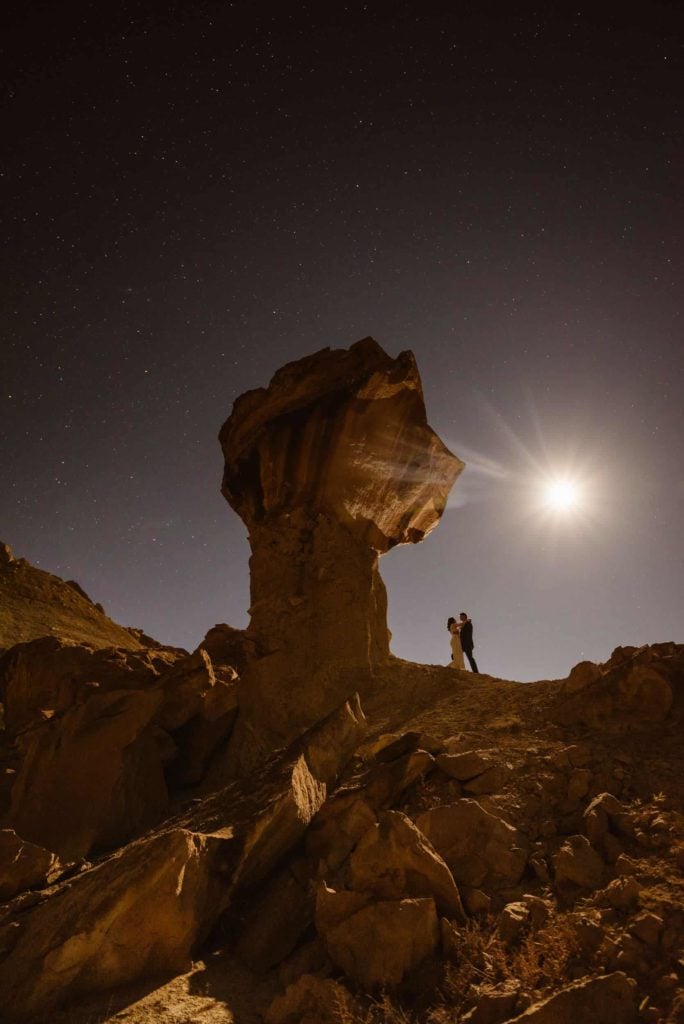 A couple stands together in a mars like landscape under the night sky. 