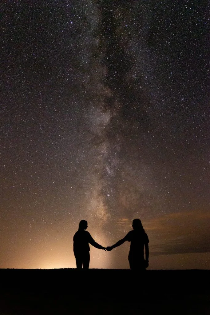 A couple holds hands under the milkyway.