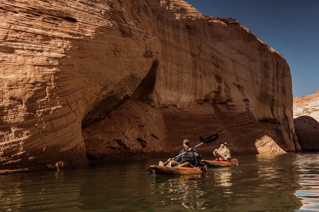 A man and woman kayak together on Lake Powell admiring the canyon walls above them. 