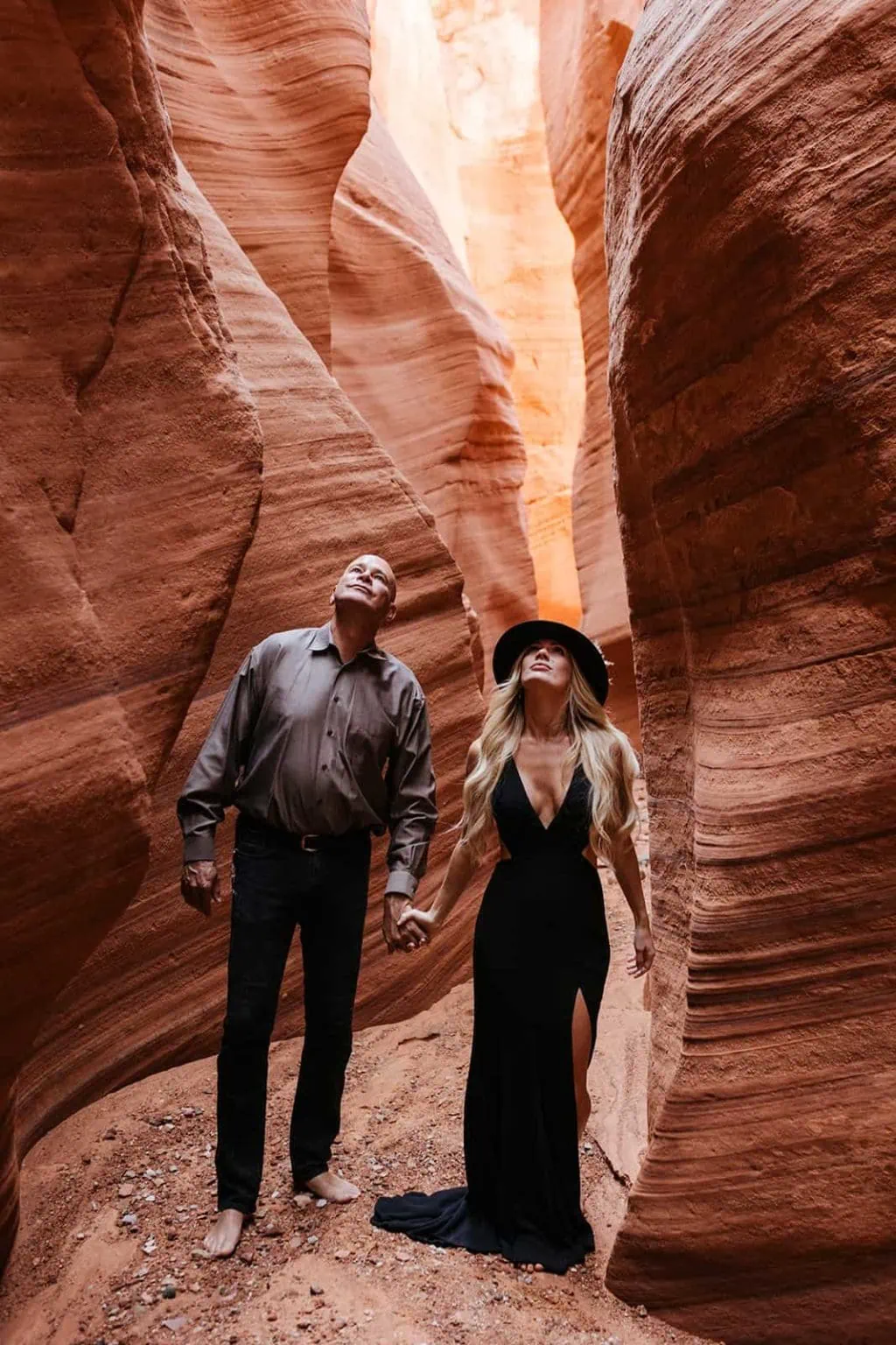 A bride and groom look up towards the top of a red rock slot canyon.