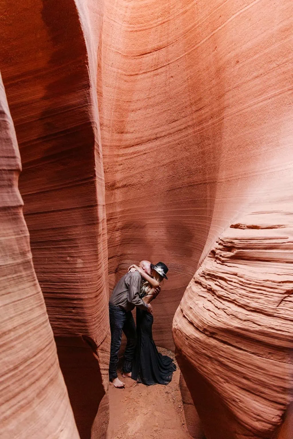 A groom kisses his bride among the walls of a red rock slot canyon.