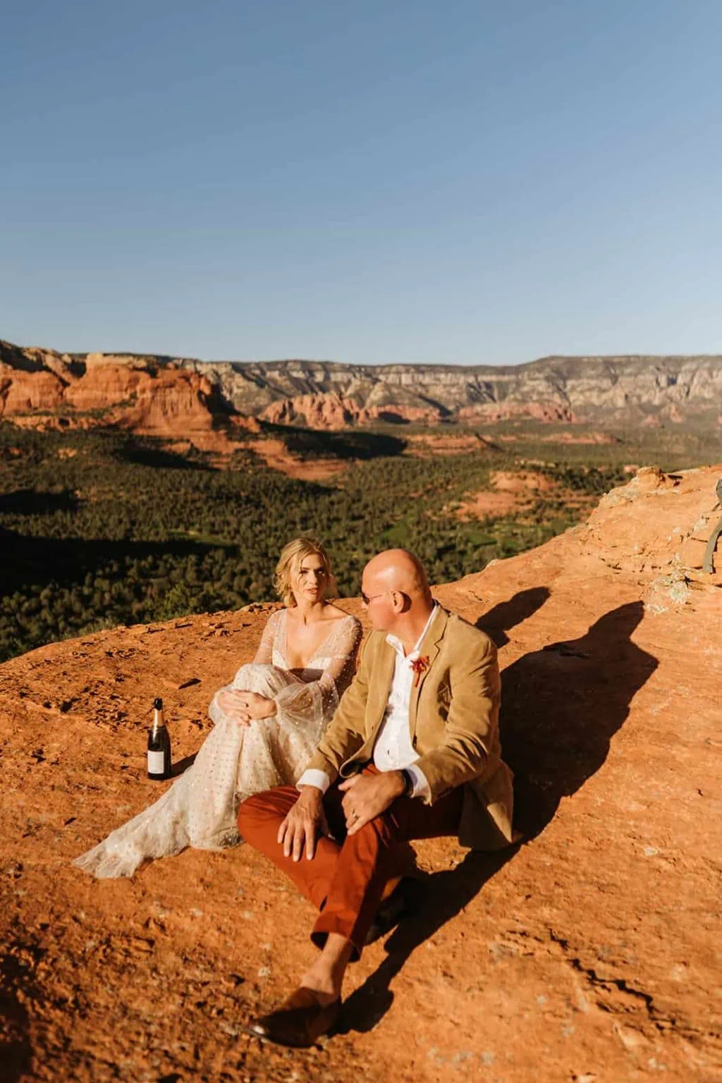 A bride and groom sit and share a bottle of champagne together in Sedona.