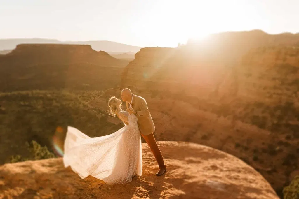 A groom goes to dip his bride back at sunset in Sedona.