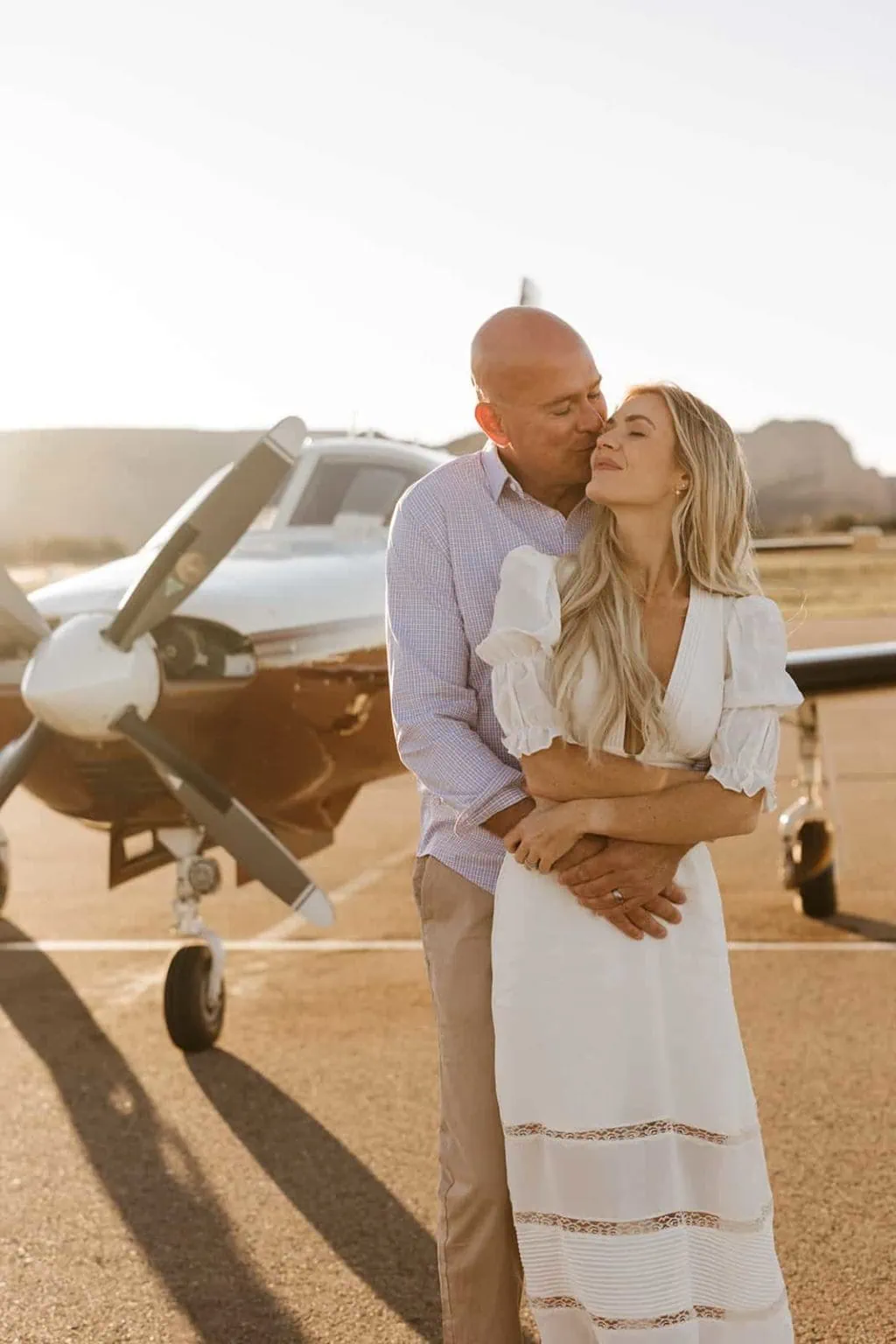 A man holds his partner in front of his airplane.
