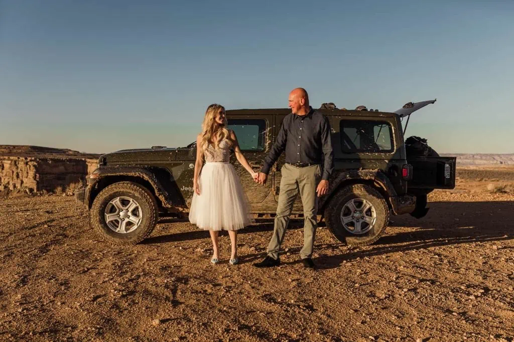 A coule holds hands standing next to their jeep.