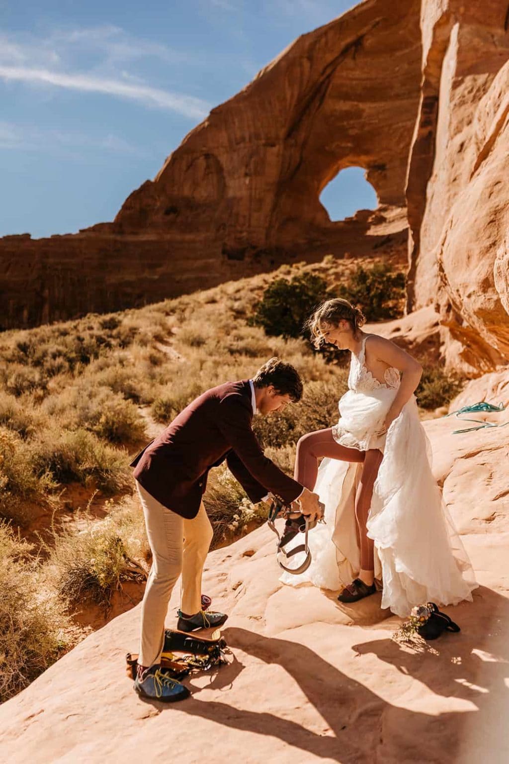 A groom helps his bride get into her climbing harness for their adventure elopement in Moab.