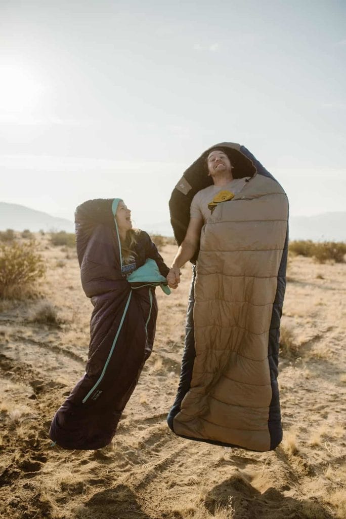 A couple jumps together in their sleeping bags as they wake up for their elopement day.