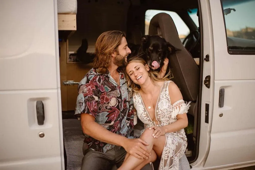 A dog licks a bride as they all sit in a van together.