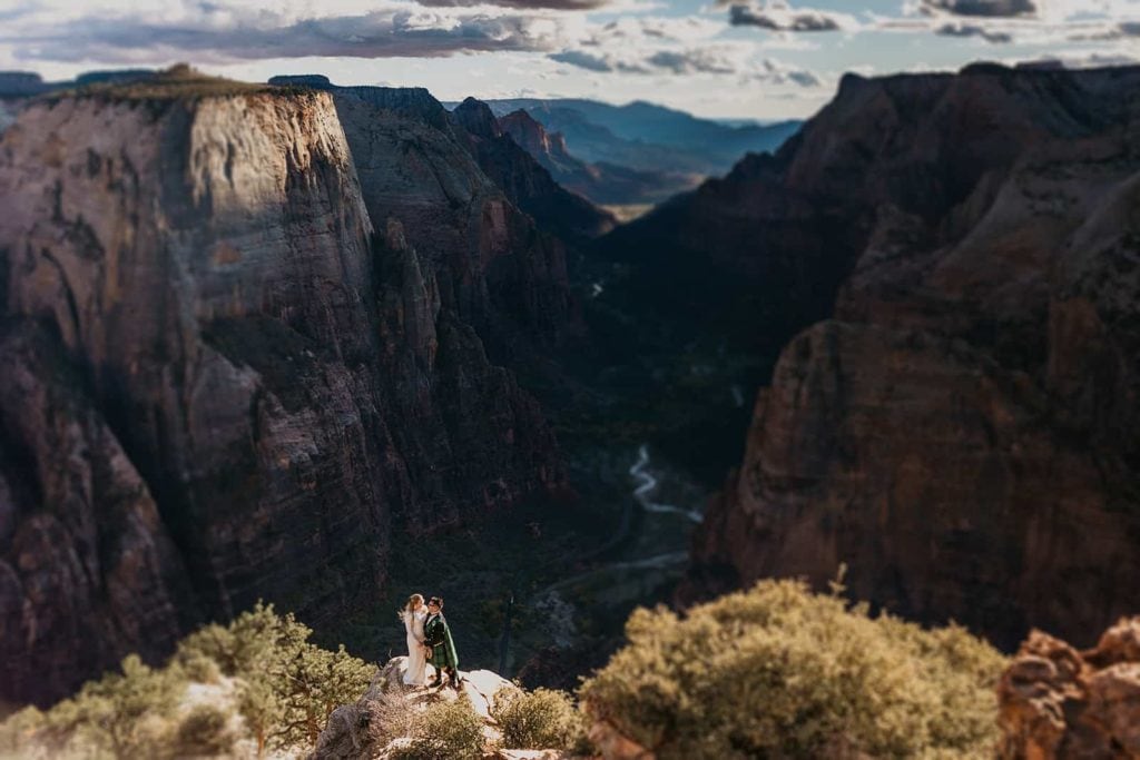A couple stands in the sun as the sun starts to set past the canyons in Zion.