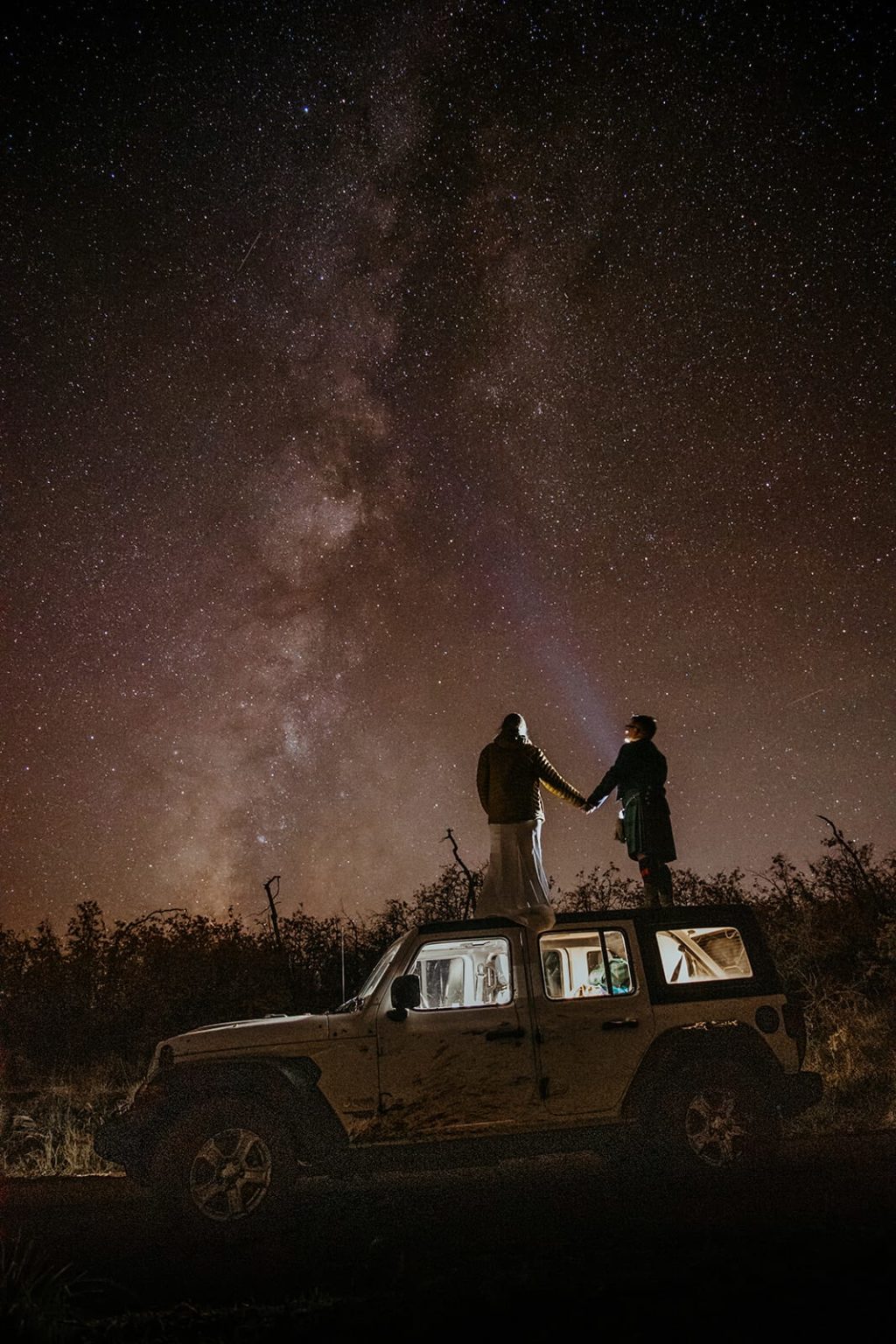 A couple admires to milky way standing on top of their jeep in Utah.