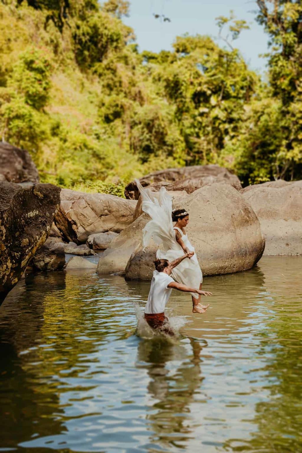 A couple jumps into a river wearing their wedding attire. 
