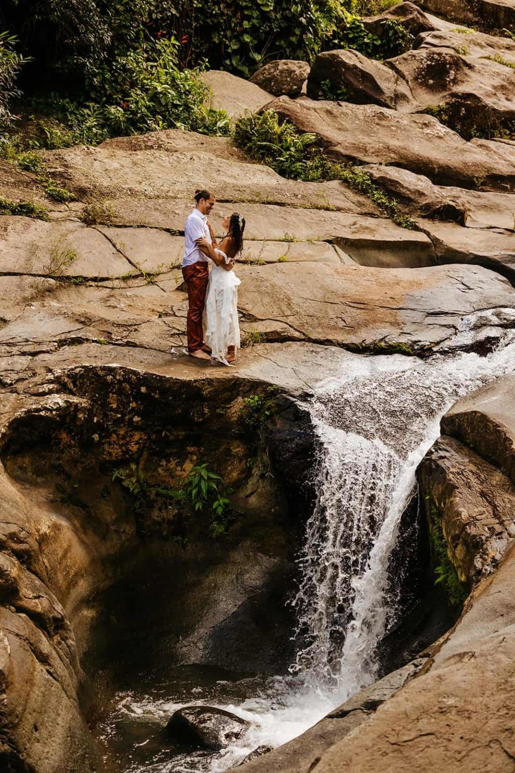 A bride and groom stare into each others eyes standing by a waterfall.