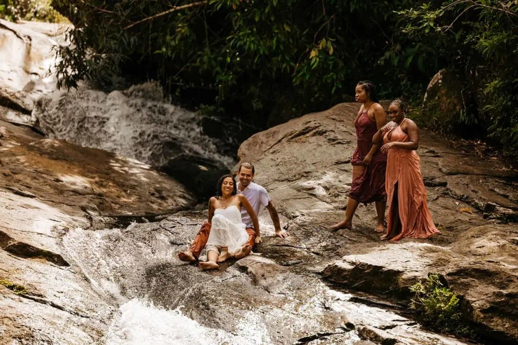A bride and groom slide down a waterfall as their bridal party watch on.