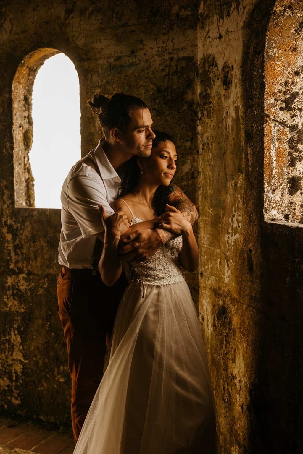 A bride and groom embrace as they look out of the window in a castle.