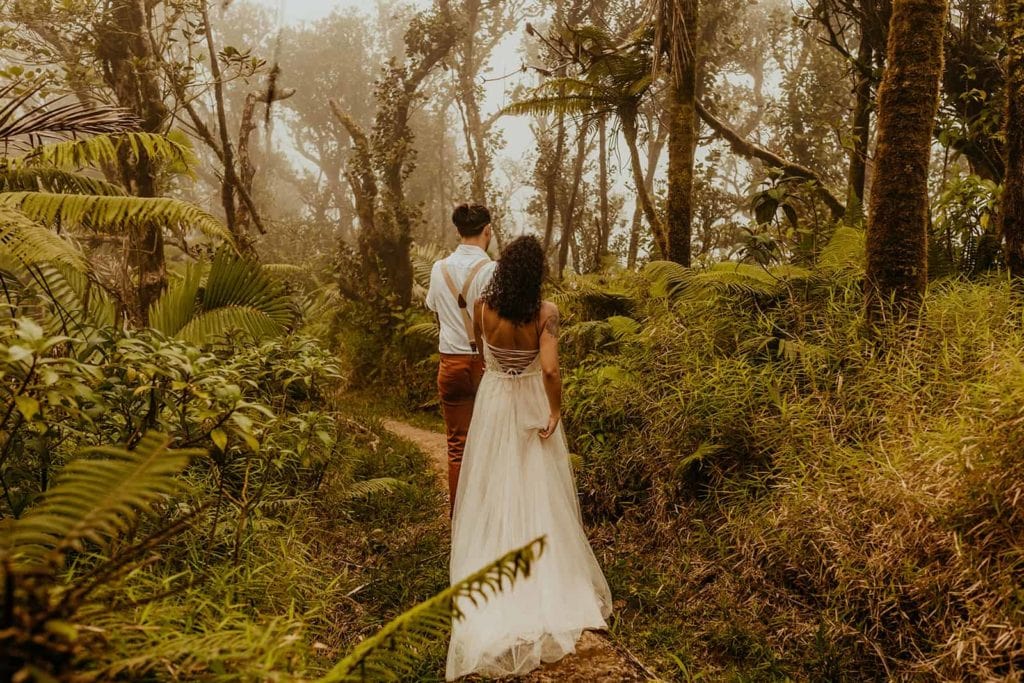 A groom leads his bride through the jungle on the trail. 