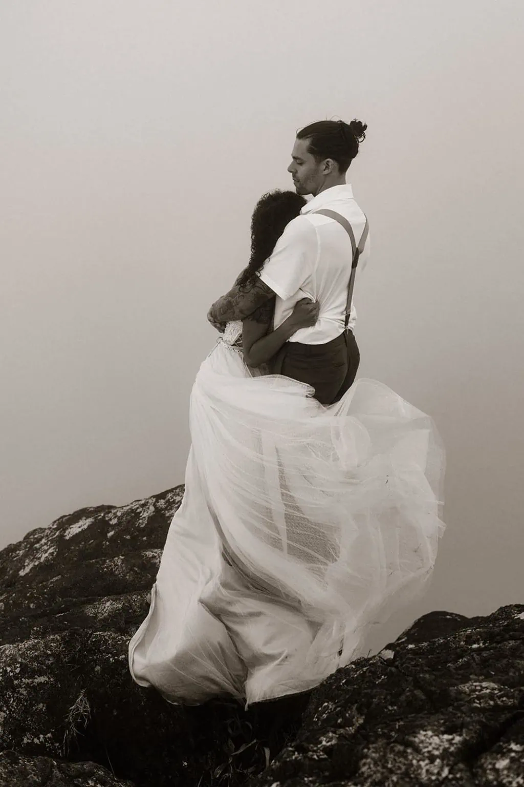 A brides dress wraps around her groom and herself because of the wind.
