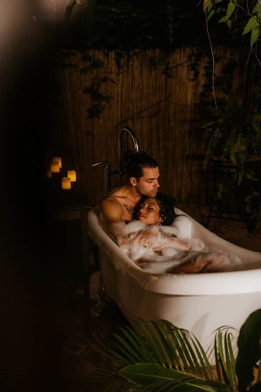 A couple hugs each other as they relax in a tub filled with bubbles. 