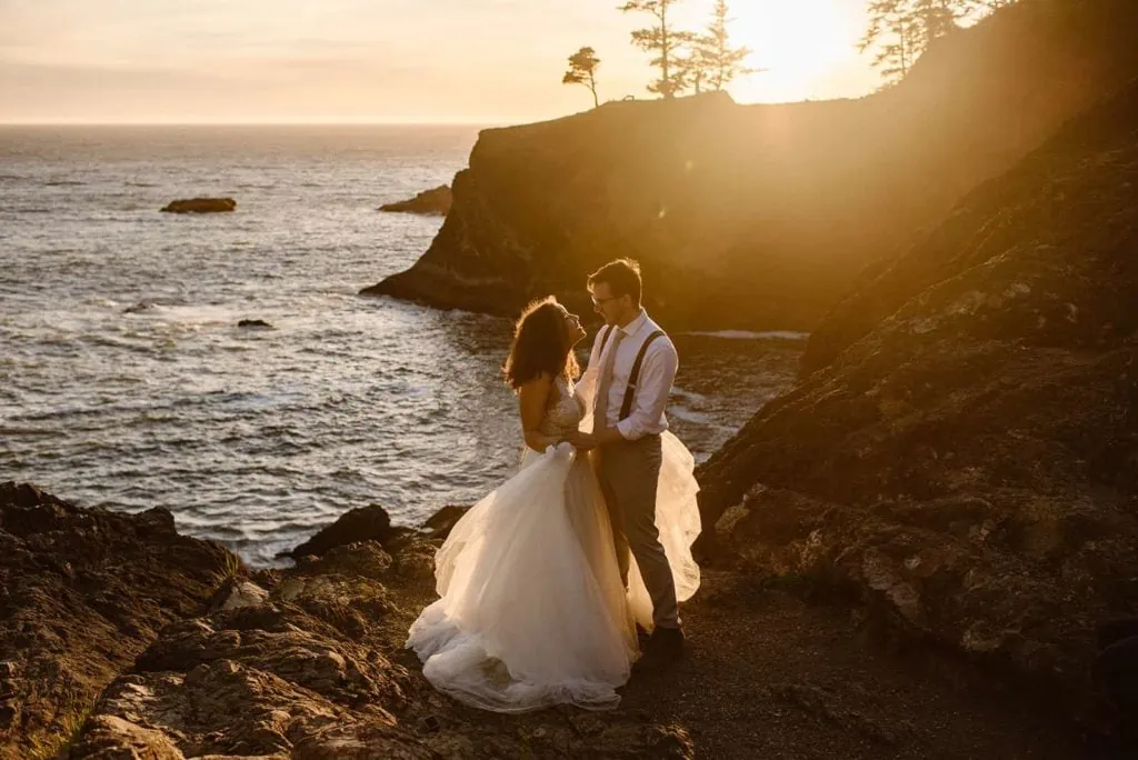 a couple embracing as they elope on the Oregon coast, overlooking the beach from the cliffs.