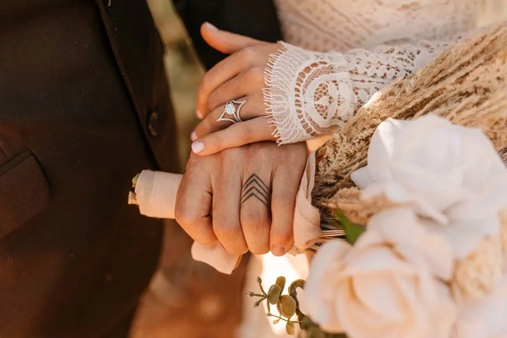 A bride and groom show off their wedding rings and wedding ring tattoos for a close up detail photograph.