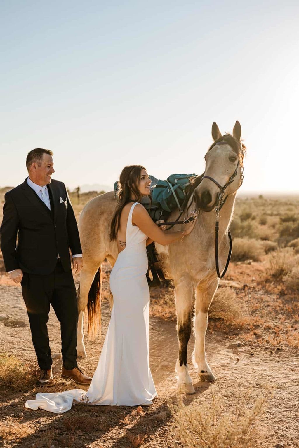 A bride smiles and pets a horse that passed her by on the trail. 