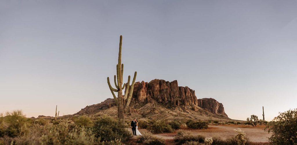 A couple stands on a hiking trail near a large cacti as they explore Lost Dutchman State Park.