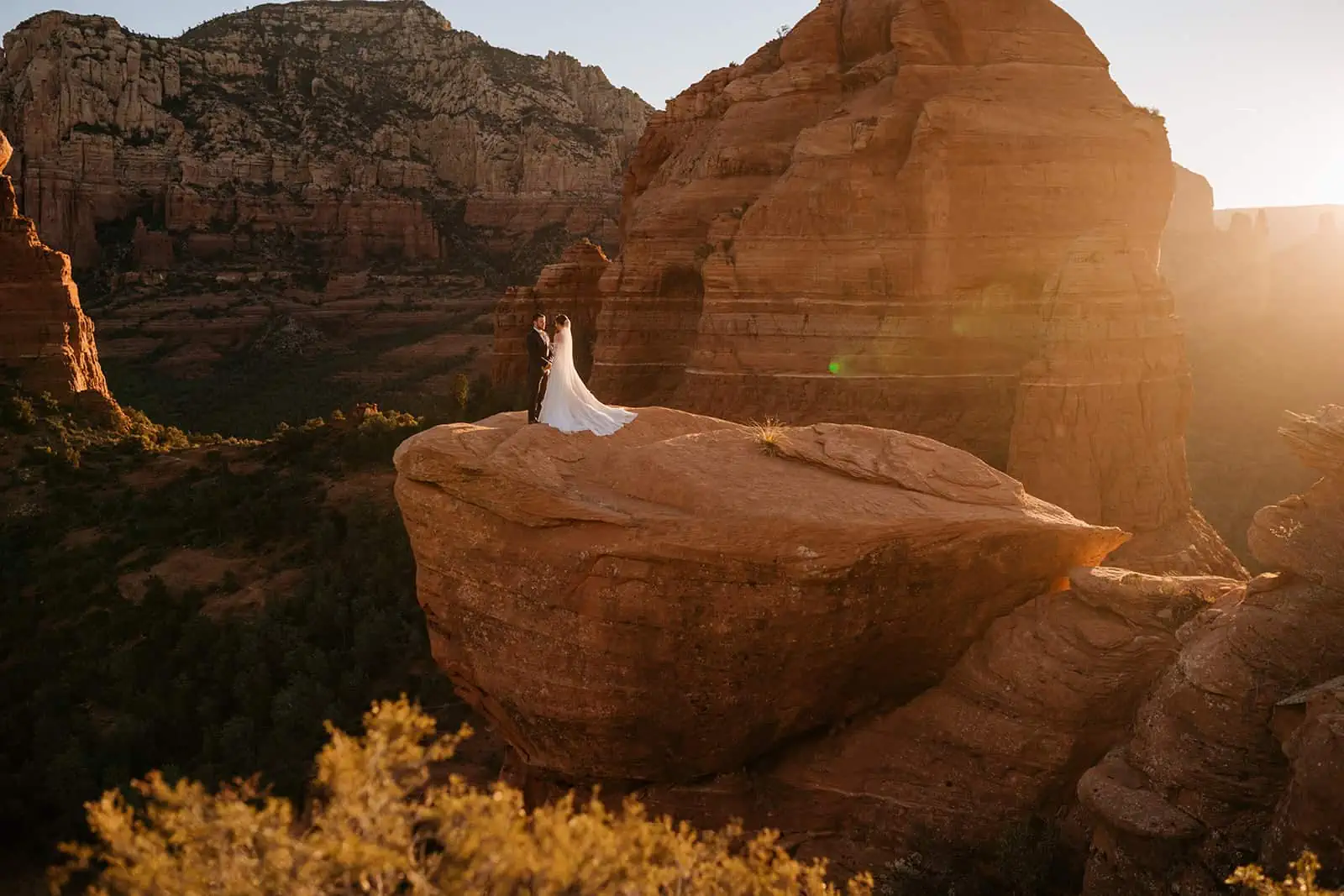 A bride and groom stand together at a vista during sunrise in Sedona.