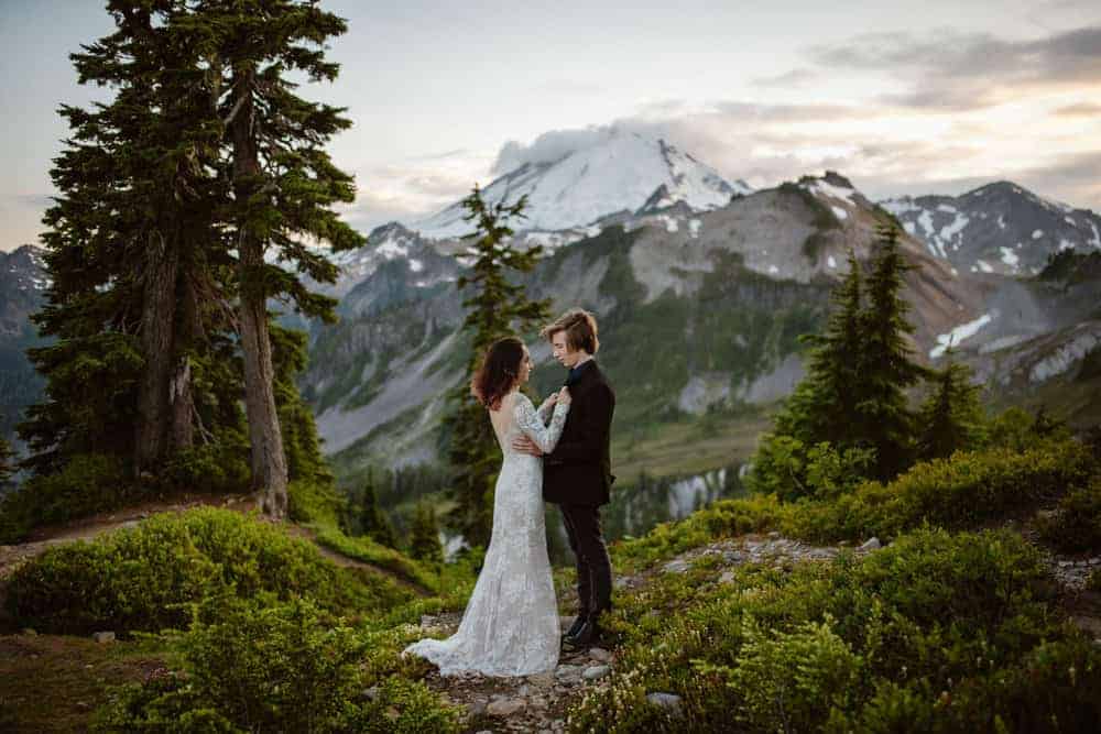 A bride and groom hold each other close as they chat together with the sun setting behind the mountains.