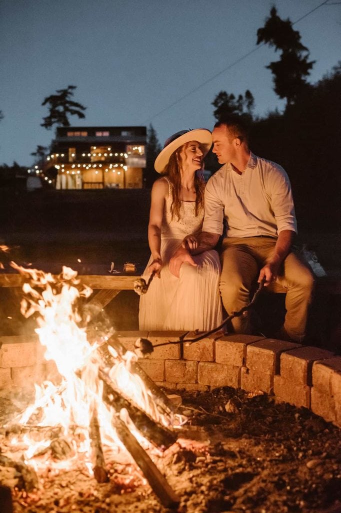 A couple roast marshmallows by the fire on a summer PNW night on their wedding day.