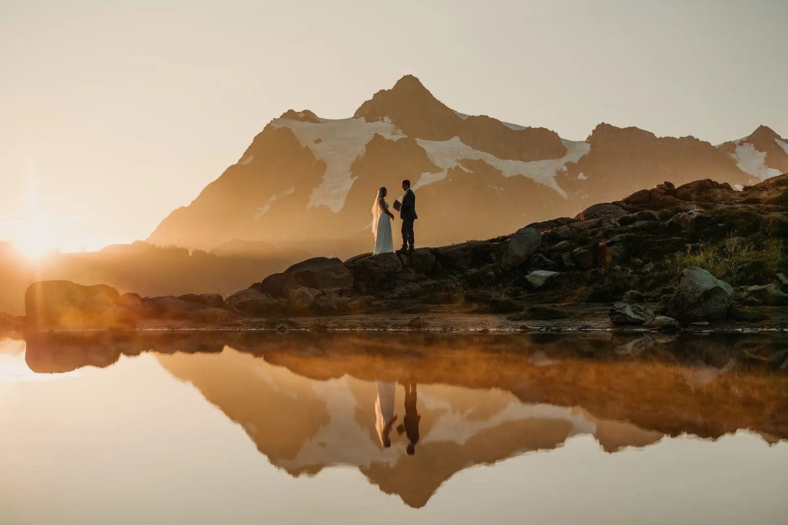 A couple shares their vows as the sun rises over the mountains.