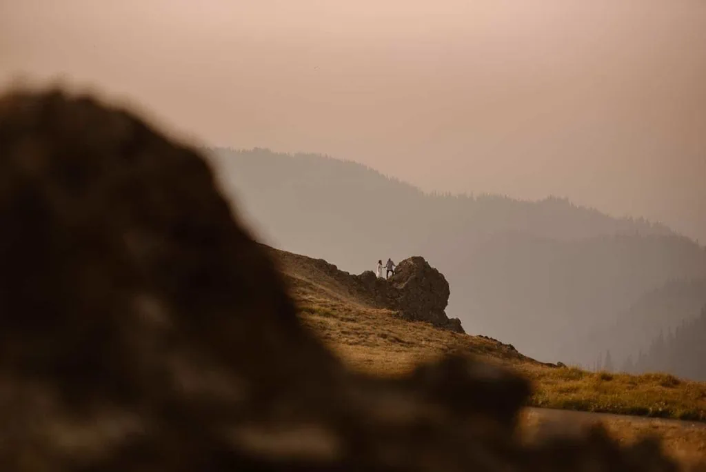 A couple stands on a rock in Olympic National Park on a smokey morning. 