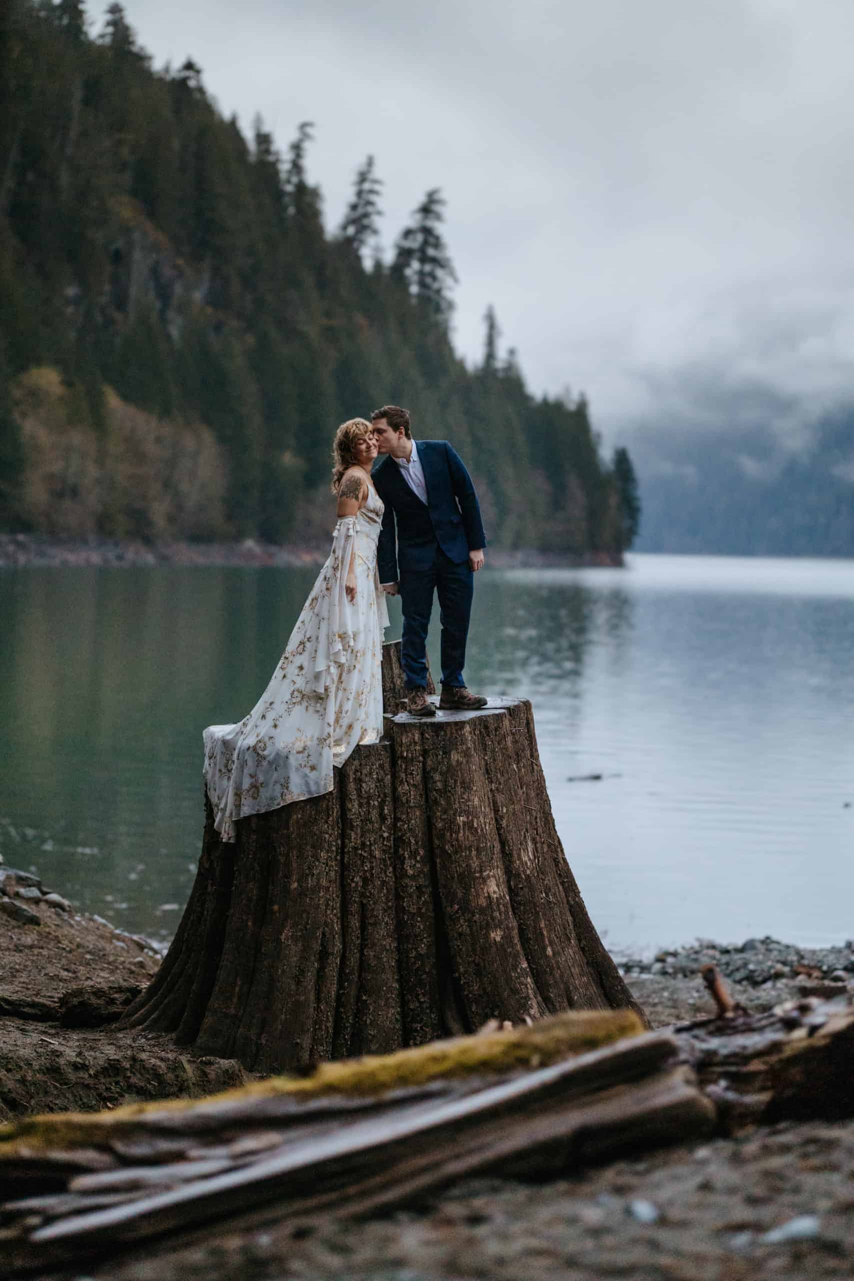 a couple kissing on a tree stump, the ocean in the background.