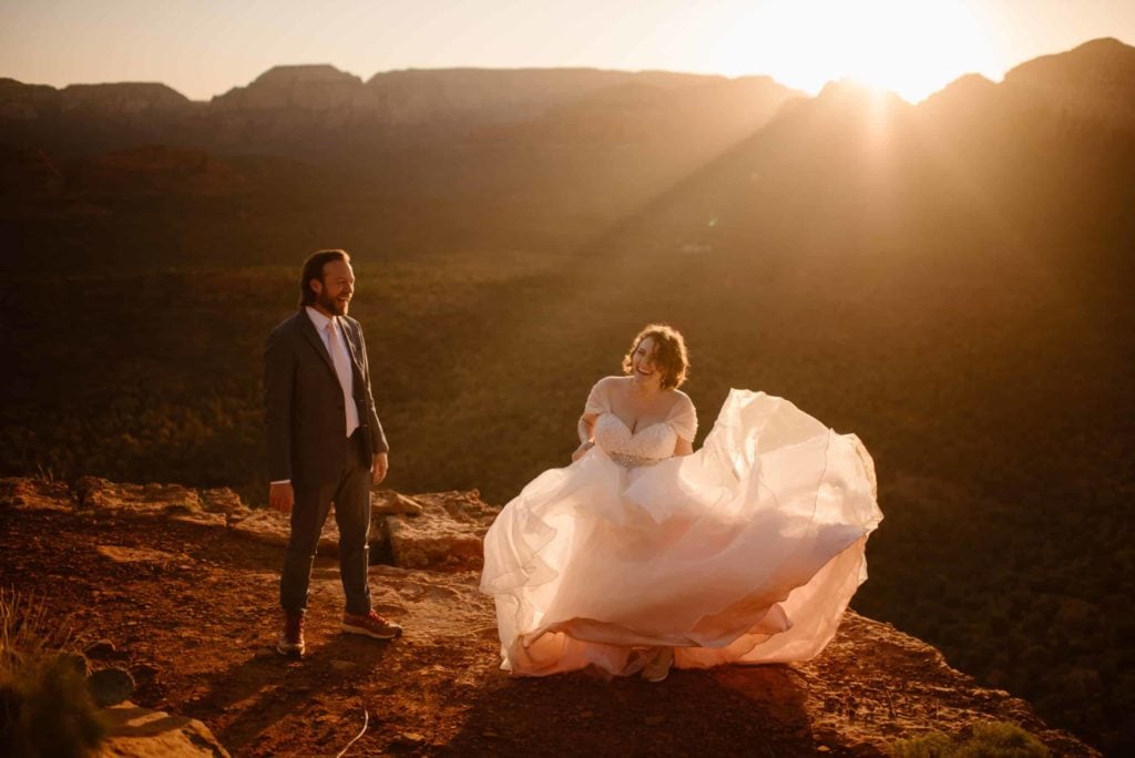 A bride dances in her ballroom wedding gown on top of a cliff in the desert.