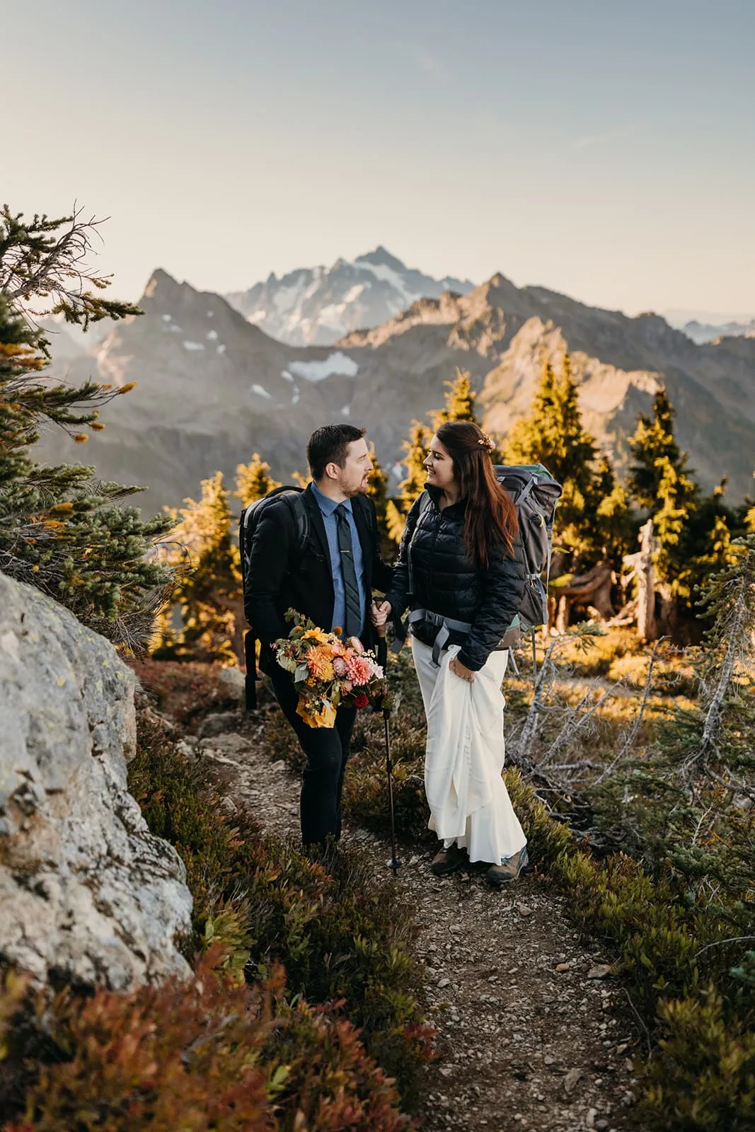 A couple smiles at each other as they hike up the mountain on the morning of their elopement.