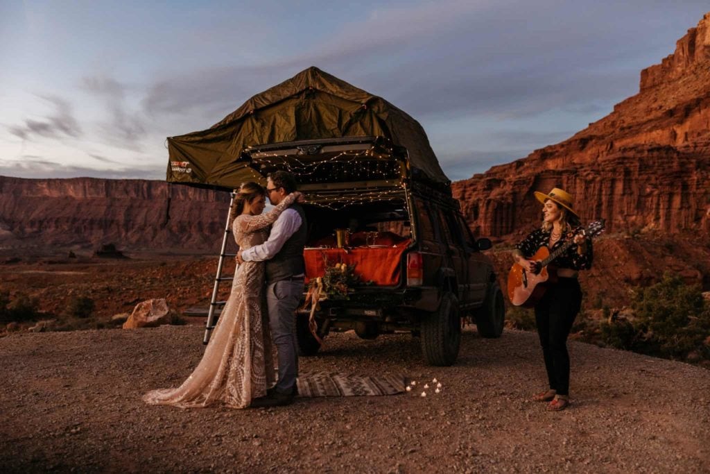 A bride and groom share their first dance together at their camp site as a friend plays guitar for them.