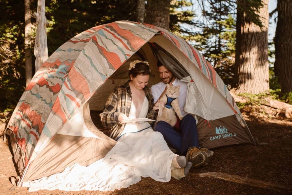 A couple sit in a tent with their cat.