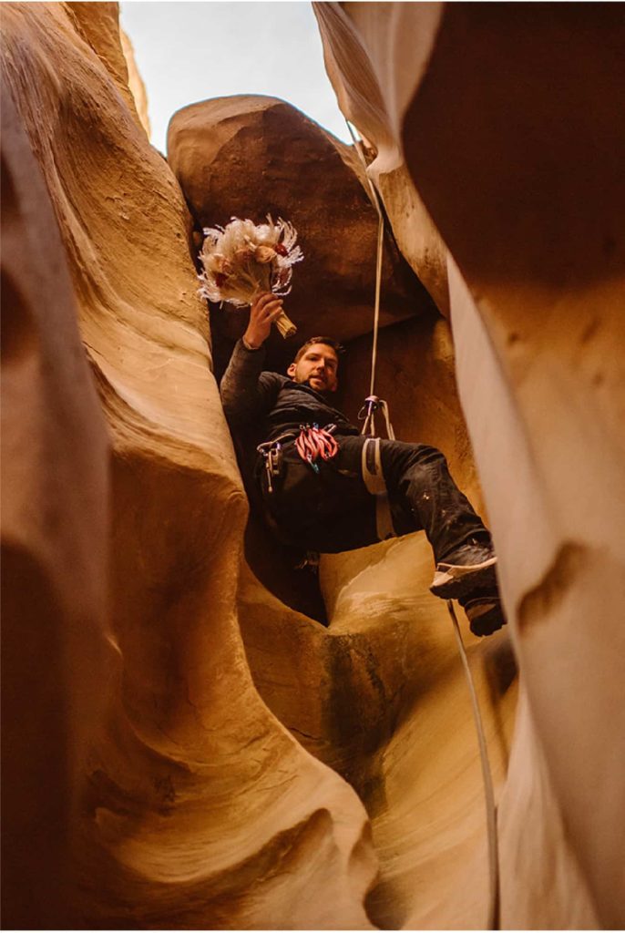 a groom rappelling down a canyon with the bride's bouquet