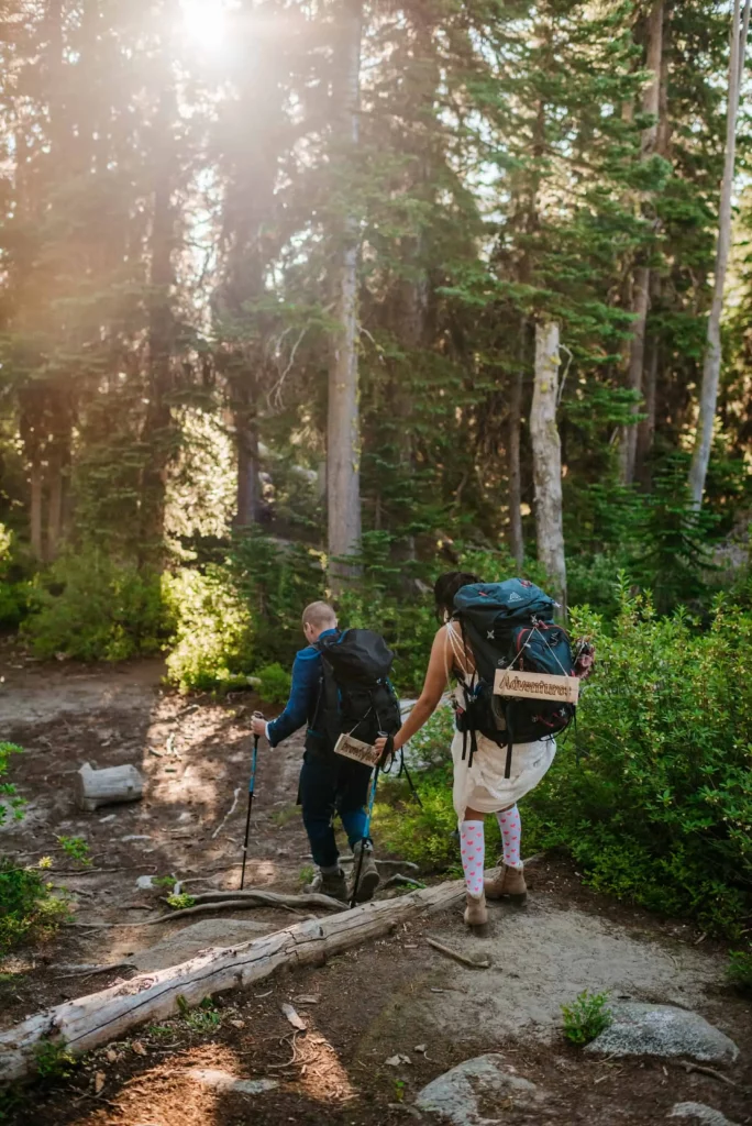 A couple hikes a trial in Leavenworth, WA in their wedding attire with their backpacks.