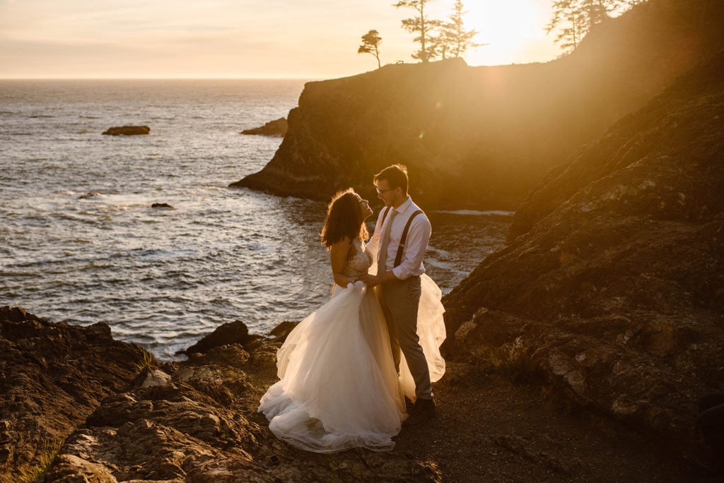 groom and bride look into each others' eyes at sunset. the ocean is behind them, lit up by the light.