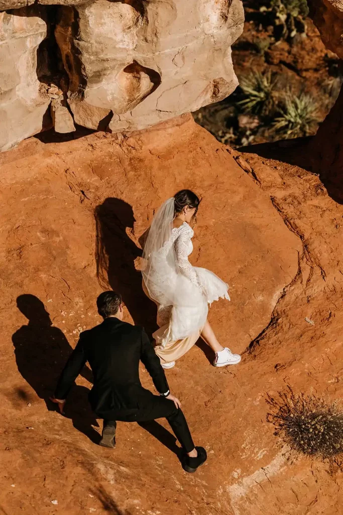 A candid image of a bride and groom walking together on a rock edge.